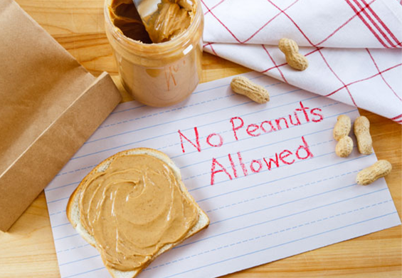 Peanut butter and peanuts on a table with a crayon drawn sign reading 'No Peanuts Allowed'